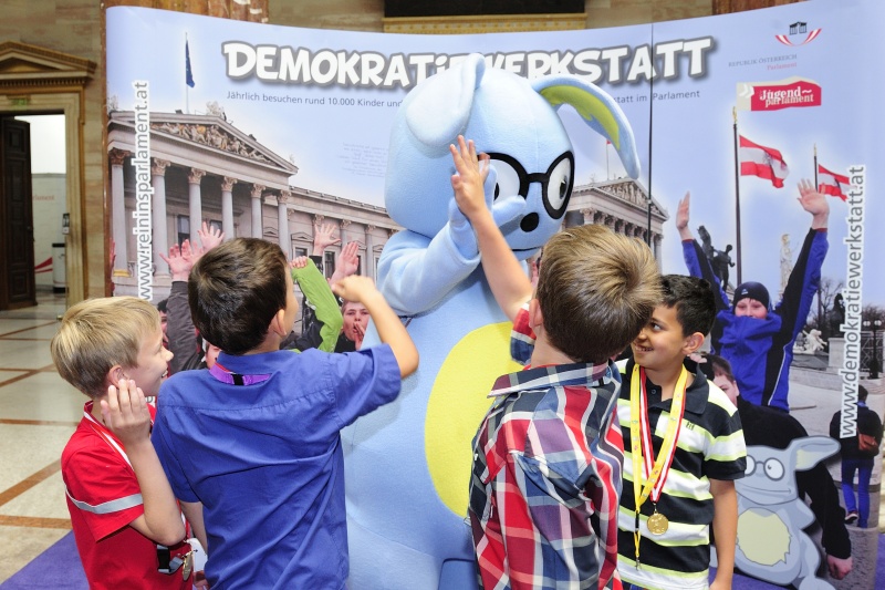 SchülerInnen mit dem Maskottchen Lesco vor dem Demokratiewerkstattplakat