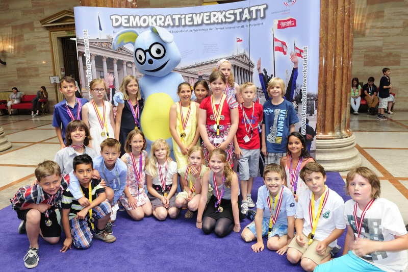 SchülerInnen mit dem Maskottchen Lesco vor dem Demokratiewerkstattplakat