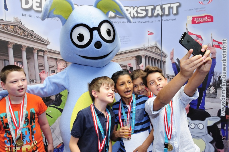 SchülerInnen mit dem Maskottchen Lesco vor dem Demokratiewerkstattplakat