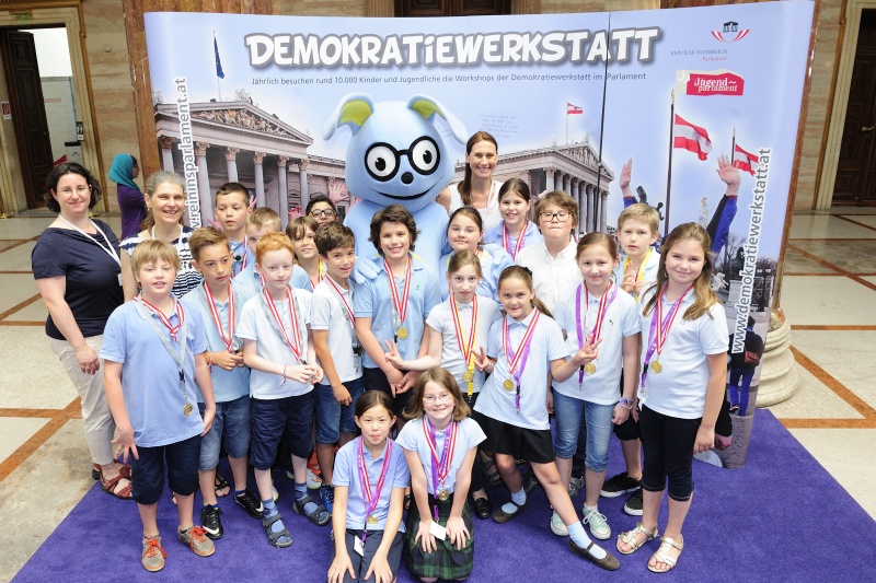 SchülerInnen mit dem Maskottchen Lesco vor dem Demokratiewerkstattplakat