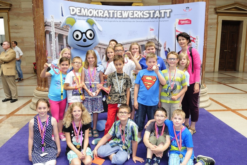 SchülerInnen mit dem Maskottchen Lesco vor dem Demokratiewerkstattplakat